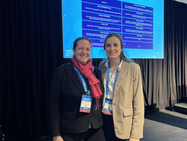 Two women standing together in front of a screen with a presentation